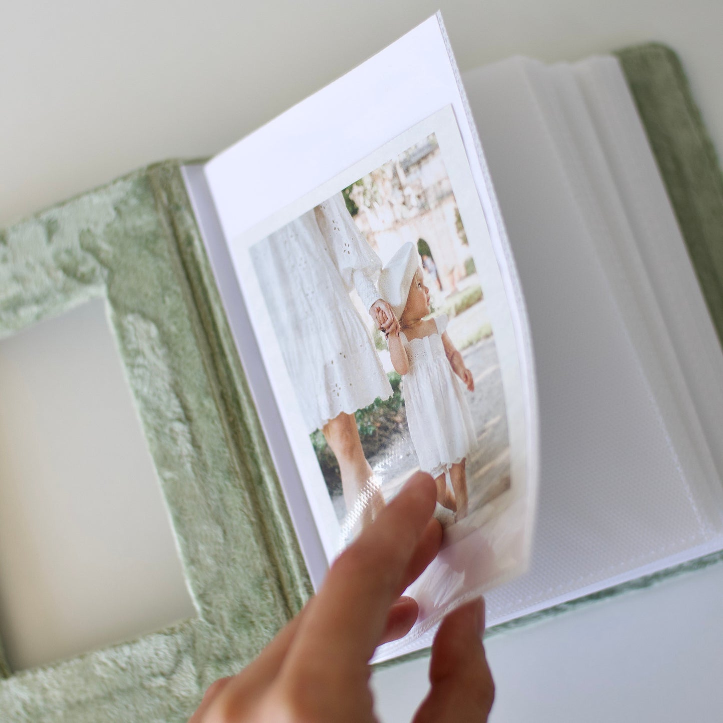 Hand holding a photo album open to a page with a picture of a person in a white dress.