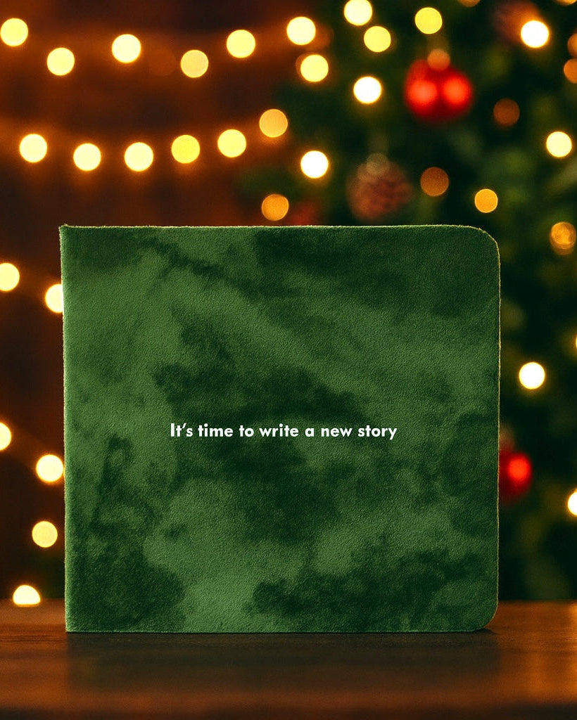 Green book with 'It's time to write a new story' text on a wooden surface with festive lights in the background