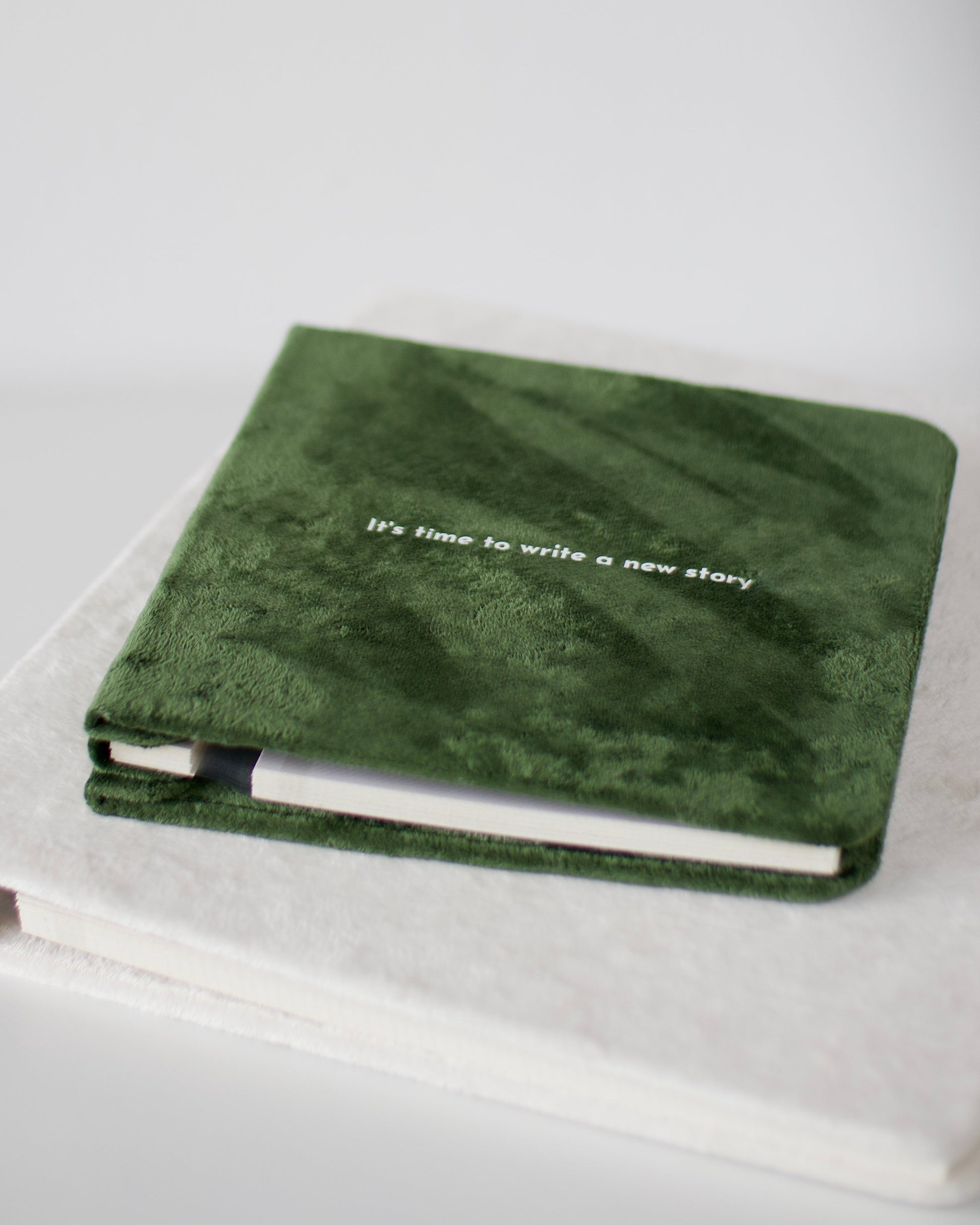 Green notebook with 'It's time to write a new story' text on a white surface